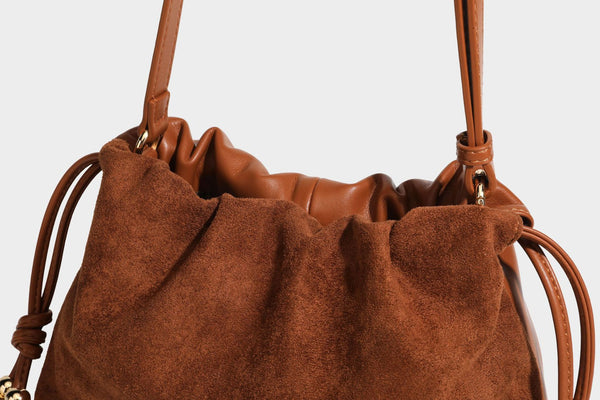 Suede-look drawstring shoulder bag in brown with smooth trim, knotted bead drawstring closure, slim adjustable strap, and