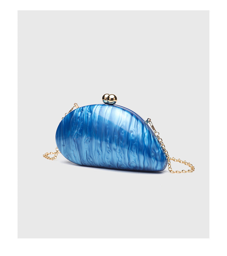 Ovale Hartschalen-Clutch in marmorierter Perlmuttoptik mit Verschluss aus zwei goldfarbenen Kugeln und goldfarbener Kettenriemen, Detailansicht