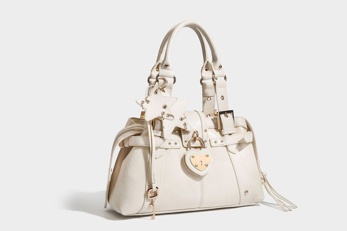 Structured leather-look satchel bag with heart padlock charm, star charm, gold-tone buckle hardware, dual top handles, and