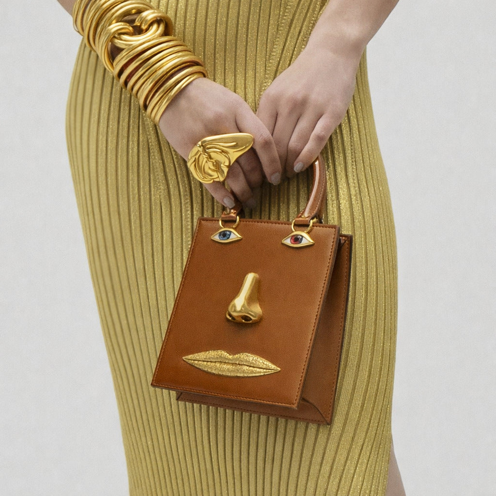 Structured rectangular top-handle bag in tan leather-look finish with gold-tone sculptural face hardware including