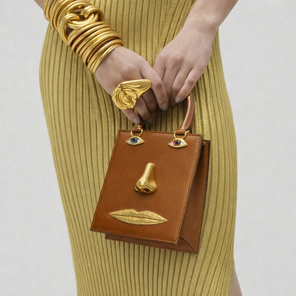 Structured rectangular top-handle bag in tan leather-look finish with gold-tone sculptural face hardware including