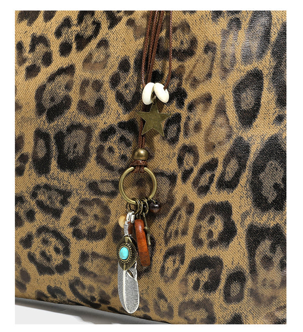 Large leopard print shoulder tote bag in tan and brown with slim dark straps and dangling beaded charm hardware, detail view