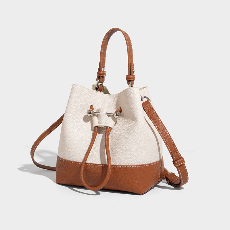 Small two-tone pebbled drawstring bucket bag with tan contrast base, metal toggle hardware, short top handle, and detachable