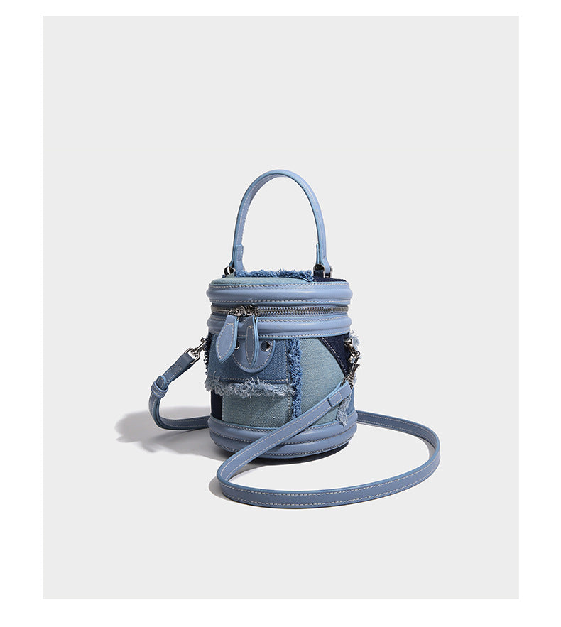 Mini cylindrical barrel bucket bag in denim patchwork with frayed edges, smooth leather-look trim, zip-around top closure