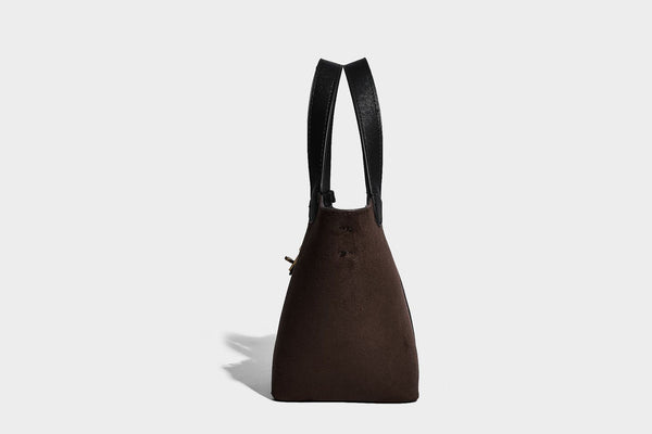 Small structured trapezoid tote bag in matte suede-look finish with black contrast trim, gold-tone front clasp, tassel charm