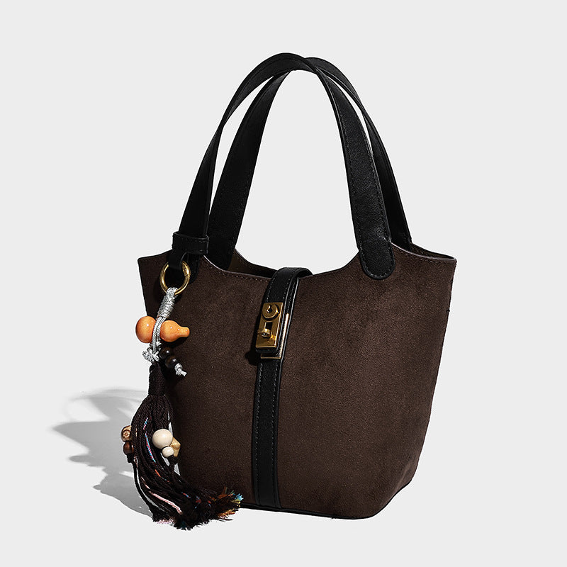 Small structured trapezoid tote bag in matte suede-look finish with black contrast trim, gold-tone front clasp, tassel charm