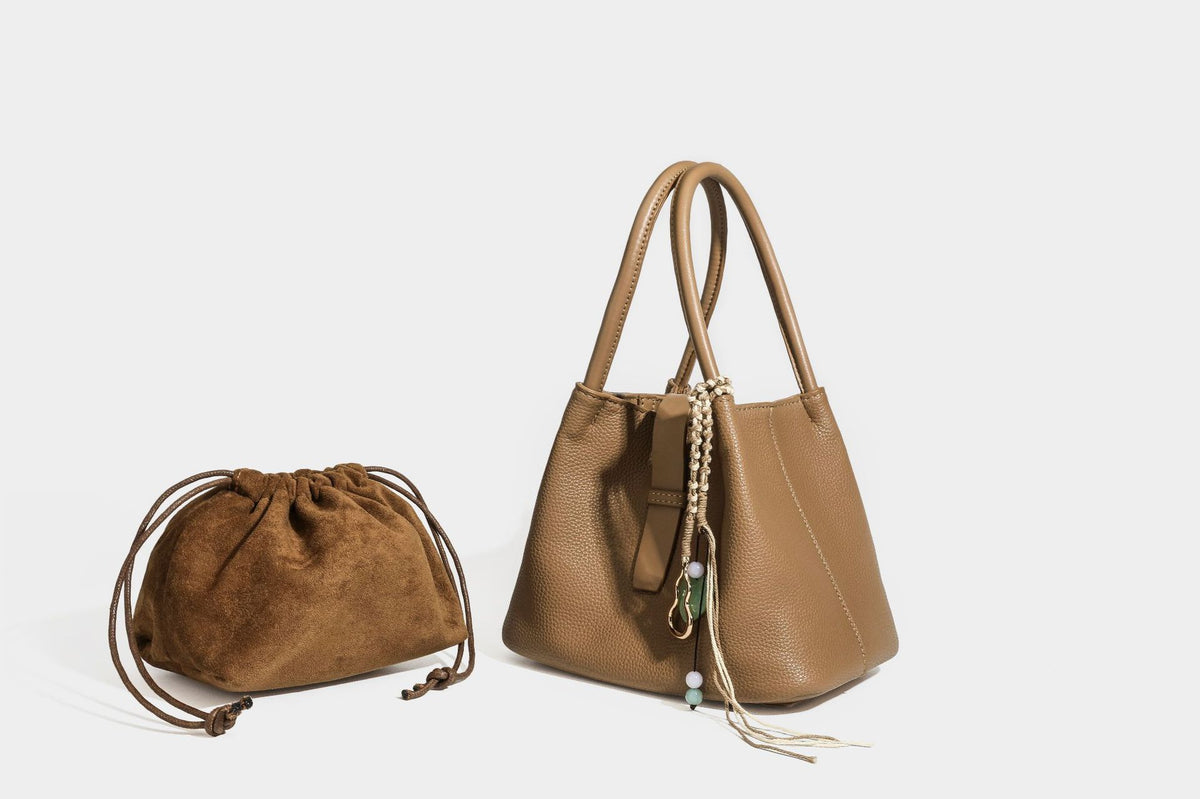 Pebbled leather-look bucket tote bag with rolled double handles, drawstring closure, braided cord charm, and detachable