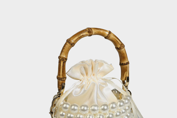 Small cylindrical bucket bag with glossy faux-pearl bead exterior, bamboo arched top handle, satin drawstring closure, and