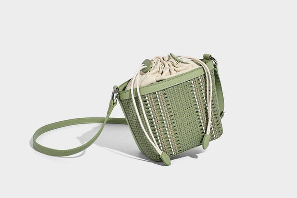 Small woven bucket bag with drawstring top, braided handle, detachable crossbody strap, and silver-tone ring hardware, detail