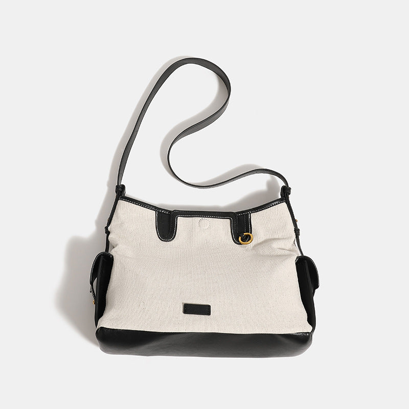 Off-white canvas shoulder bag with black leather-look trim, gold-tone ring hardware, top zip closure, side flap pocket, and
