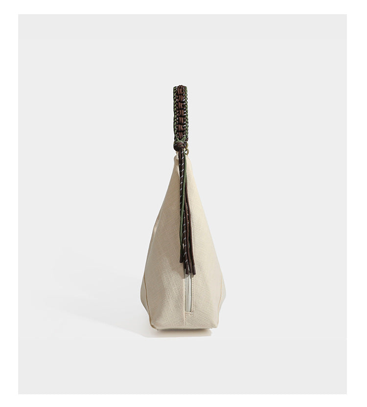 Soft slouchy cream canvas shoulder tote with braided brown and green cord handle, gold-tone ring hardware, and tassel trim