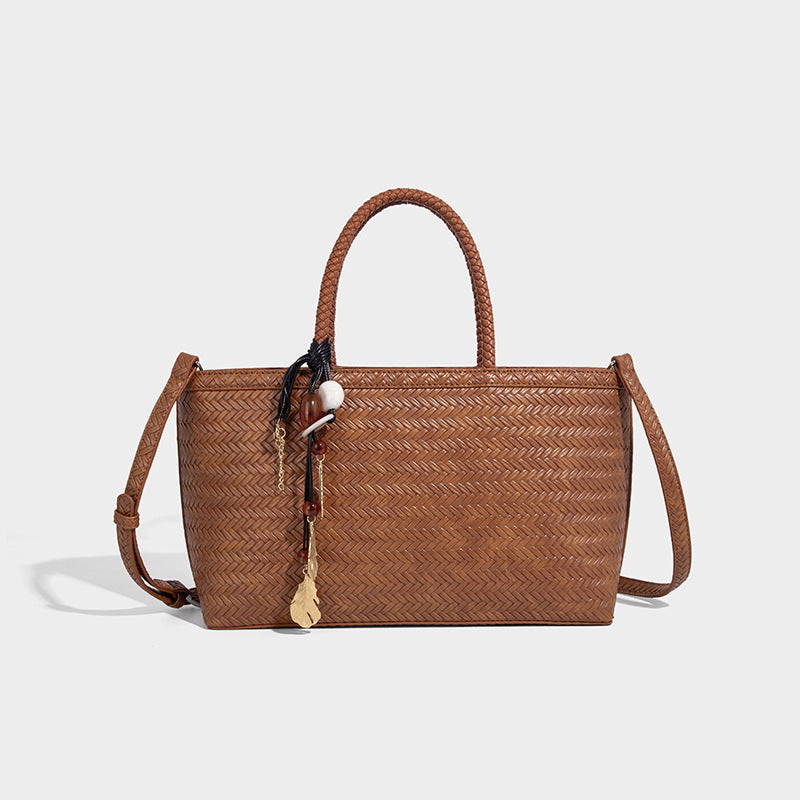 Structured woven-texture tote bag with brown braided top handles, decorative tassel charm, and detachable shoulder strap