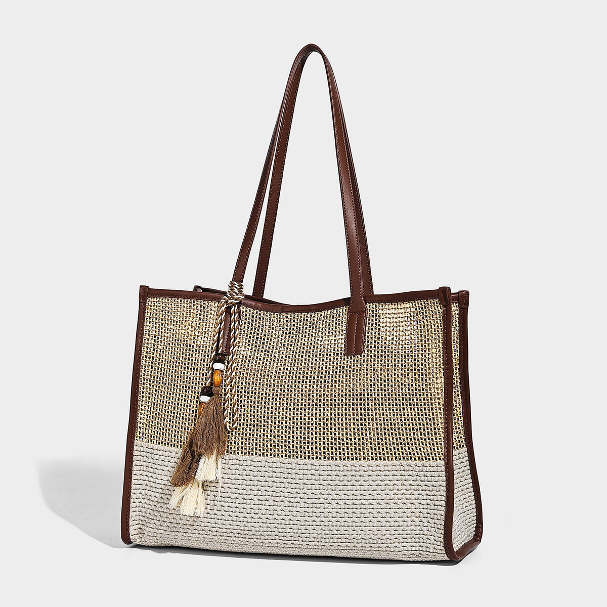 Large open-weave straw tote bag in tan and cream with dark brown leather-look trim, long shoulder straps, and a beaded