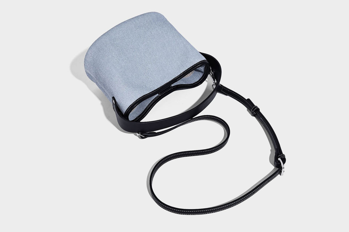 Hellblaue Bucket-Bag aus Denim mit schwarzem Besatz in Lederoptik, silberfarbenen Beschlägen, kurzem Tragegriff und langem verstellbarem Crossbody-Riemen