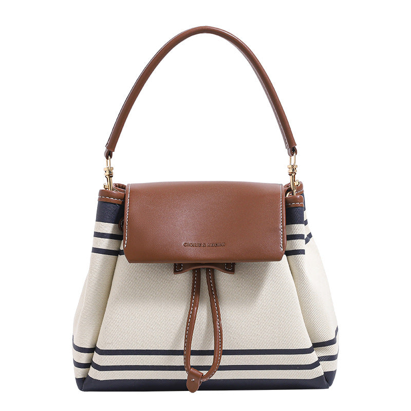 Cremefarbene Canvas-Beuteltasche mit marineblauen horizontalen Streifen, cognacfarbenem Kunstleder-Lappen und -Besatz, goldfarbenen Metalldetails und wandelbarer Trageweise