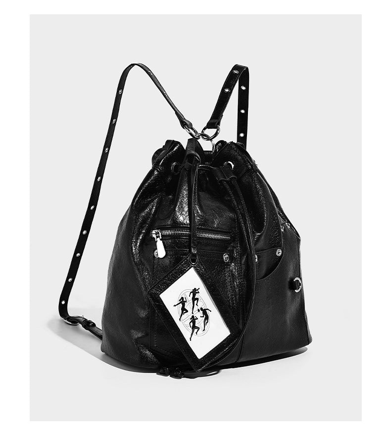 Glossy black convertible bucket backpack with silver grommet-studded straps, drawstring cinch closure, and front zip pocket