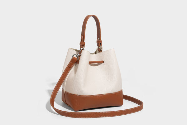 Small two-tone pebbled drawstring bucket bag with tan contrast base, metal toggle hardware, short top handle, and detachable