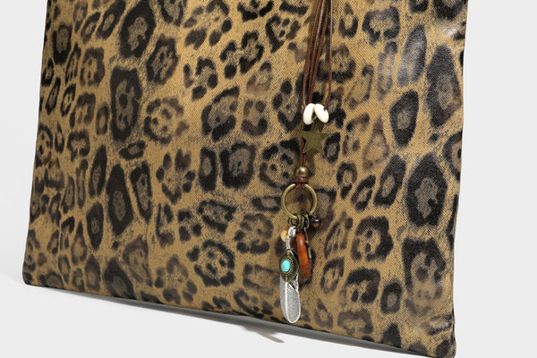 Large leopard print shoulder tote bag in tan and brown with slim dark straps and dangling beaded charm hardware, detail view