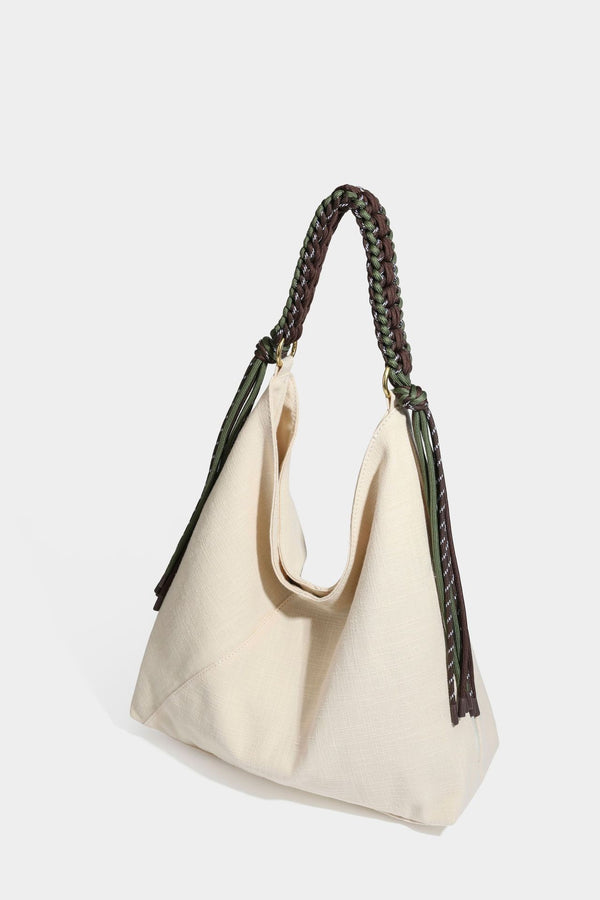 Soft slouchy cream canvas shoulder tote with braided brown and green cord handle, gold-tone ring hardware, and tassel trim