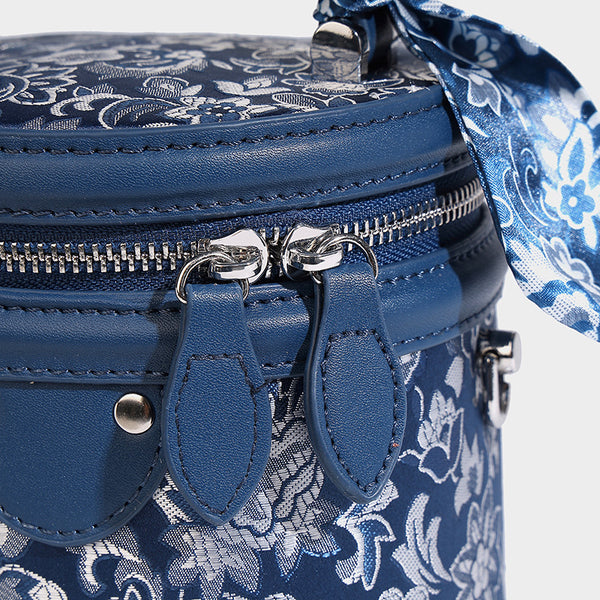 Small cylindrical barrel bag in blue-and-white floral jacquard with leather-look trim, scarf-wrapped top handle, silver-tone