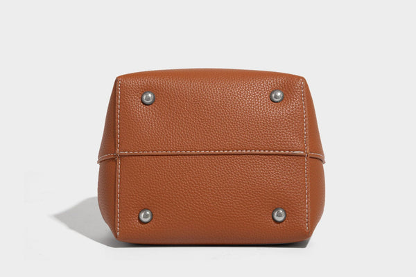 Small two-tone pebbled drawstring bucket bag with tan contrast base, metal toggle hardware, short top handle, and detachable