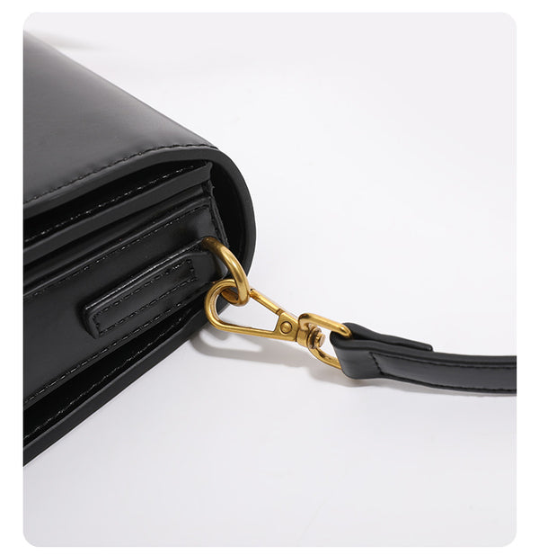 Mini structured black flap crossbody bag with gold-tone ribbed rectangular clasp and adjustable shoulder strap, detail view
