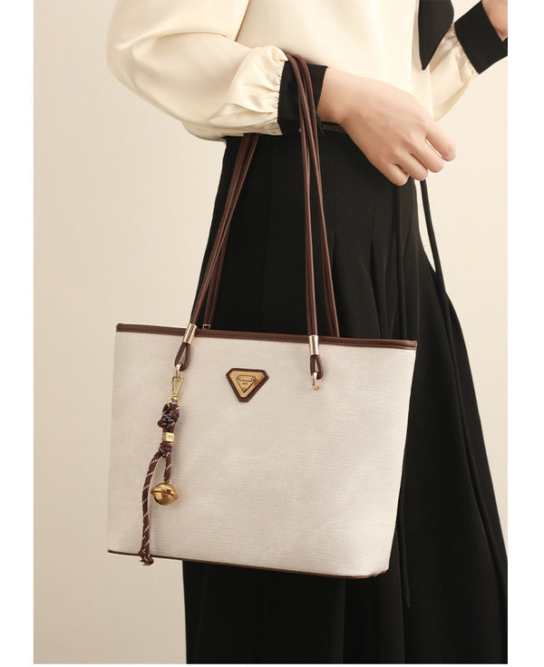 Große, strukturierte Tote-Bag mit offenem Oberteil in Creme, dunkelbrauner Borte in Lederoptik, zwei Schulterriemen und dreieckigem Logo-Badge