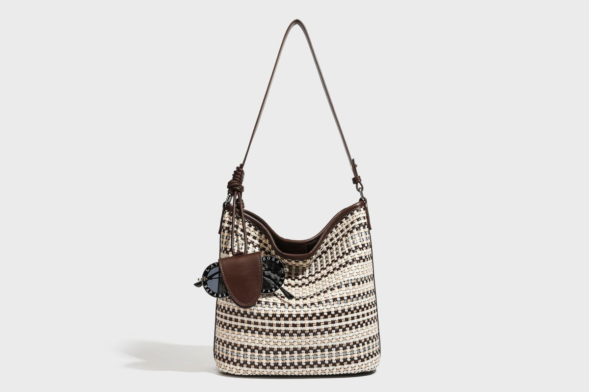 Woven stripe bucket shoulder bag in cream and dark brown with leather-look trim, knotted adjustable strap, and small shield