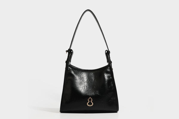 Strukturierte, trapezförmige Schultertasche aus glänzender, geknautscht wirkender Lederoptik mit goldfarbenen Beschlägen auf der Vorderseite und langem, verstellbarem