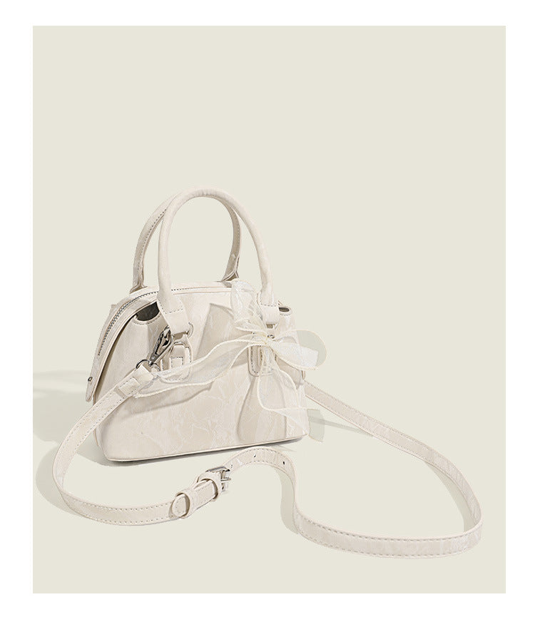 Small structured Boston bag in cream with glossy crinkled finish, sheer bow accent, silver-tone hardware, dual top handles