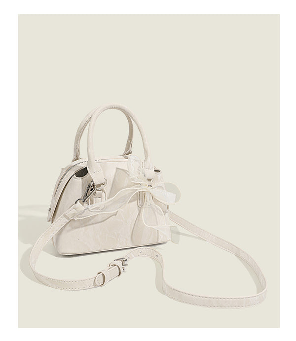 Small structured Boston bag in cream with glossy crinkled finish, sheer bow accent, silver-tone hardware, dual top handles