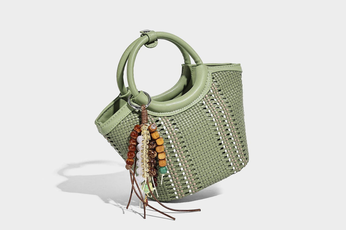 Kleine strukturierte Beuteltasche aus geflochtenem Material mit rundem Tragegriff in Lederoptik, silberfarbenen Beschlägen und perlenbesetztem Quastenanhänger, Detail