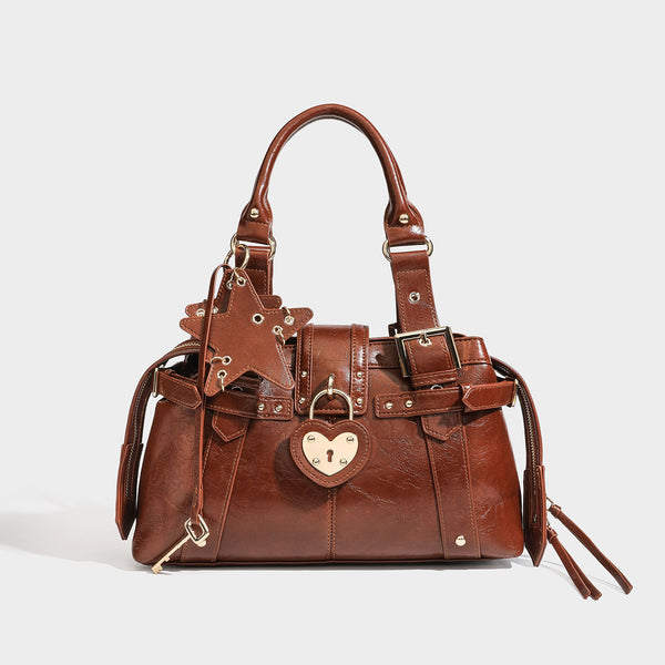 Structured leather-look satchel bag with heart padlock charm, star charm, gold-tone buckle hardware, dual top handles, and