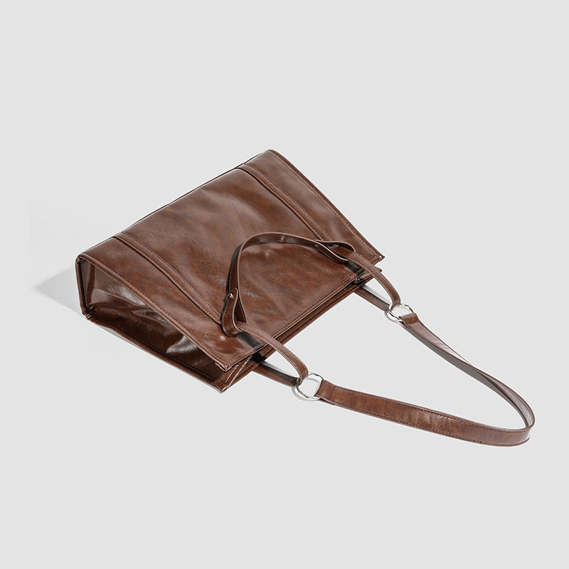 Large structured glossy leather-look tote bag with dual top handles and long shoulder strap in burnished brown, detail view 3