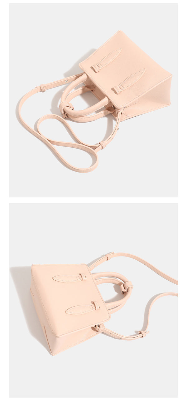 Small structured trapezoid top-handle bag in pebbled matte finish with decorative strap tabs, twin knotted handles, and