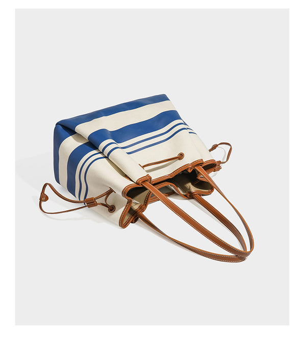 Large cream and navy striped canvas bucket tote bag with tan leather-look trim, drawstring closure, and double shoulder