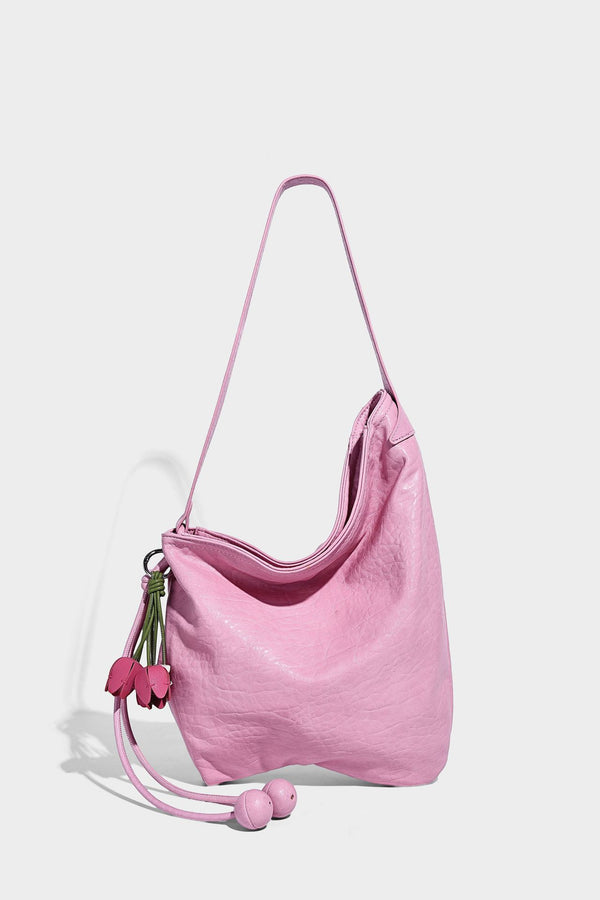 Slouchy hobo shoulder bag in pale yellow with slim strap, drawstring bead closure, and pink tulip floral charm, detail view