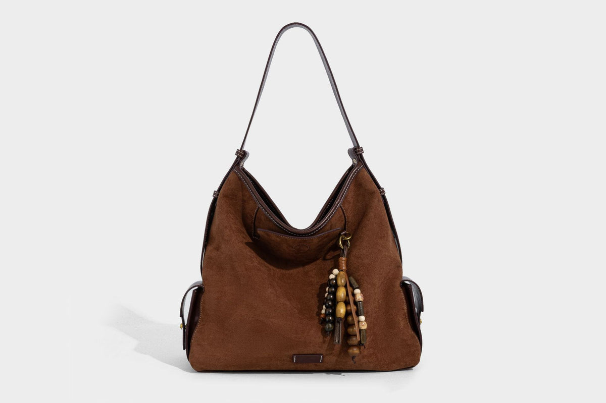 Weich fallende Hobo-Schultertasche in Khaki mit matter Velourslederoptik, Besatz in dunkelbrauner Lederoptik, Quastenanhänger mit Perlen und seitlicher Klappe, Detailansicht