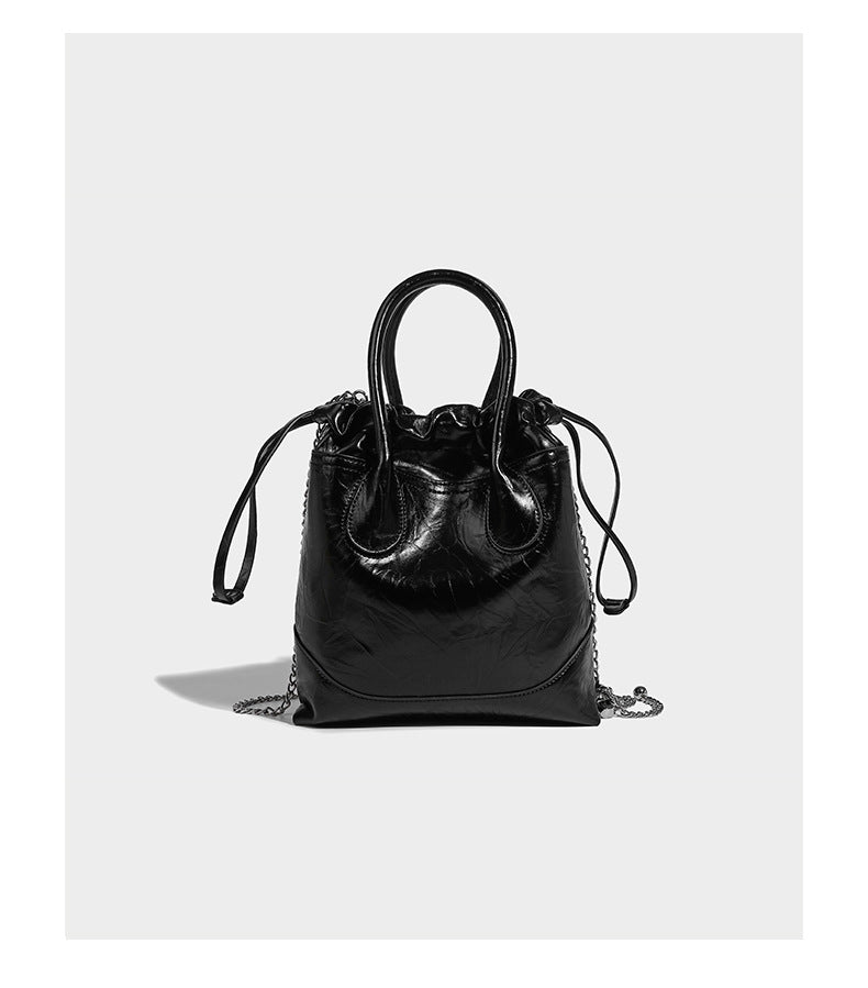 Glossy crinkled ruched drawstring bucket bag with rounded double top handles and detachable chain crossbody strap, detail