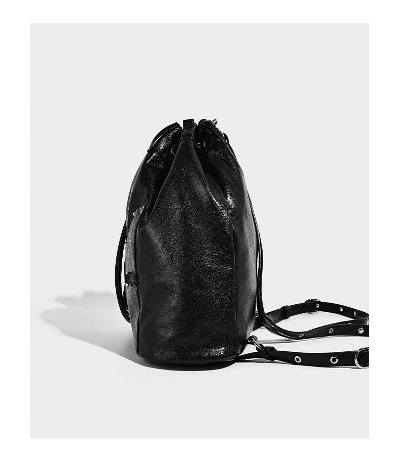 Glossy black convertible bucket backpack with silver grommet-studded straps, drawstring cinch closure, and front zip pocket