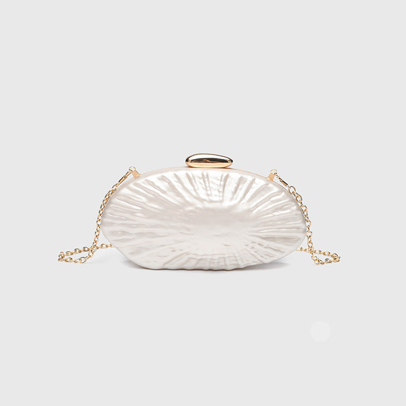 Oval pearl-finish shell clutch bag with gold-tone clasp and removable gold link chain strap, front view