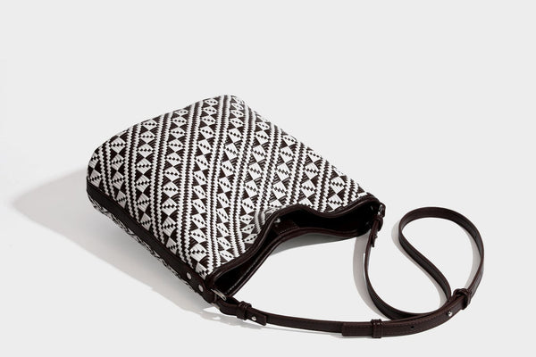 Geflochtene Schultertasche mit geometrischem Ethno-Muster, Besatz in dunkelbrauner Lederoptik, langem verstellbarem Träger und kleinem hängendem Reißverschluss
