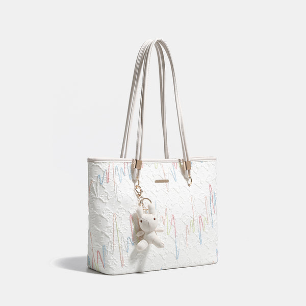 Off-white structured tote bag with dual shoulder straps, gold-tone hardware, and plush bear charm, detail view 3