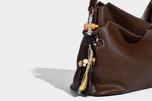 Large slouchy leather-look hobo tote bag with open top, adjustable shoulder strap, and colorful tassel bead charm, detail