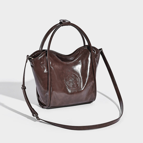 Glossy leather-look structured tote bag with rounded top handles, detachable shoulder strap, embossed front emblem, and side