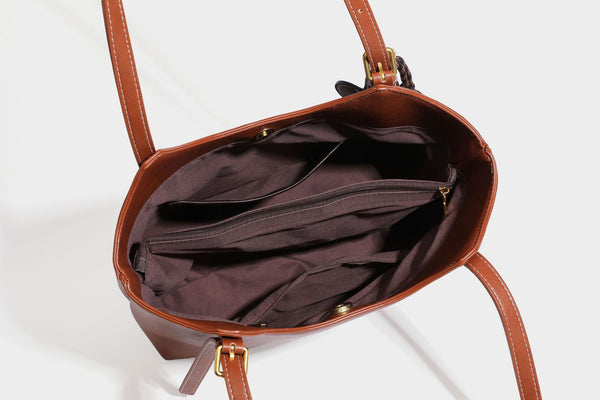 Structured smooth leather-look tote bag with long shoulder strap, gold-tone hardware, and hanging tassel-coin charm, detail