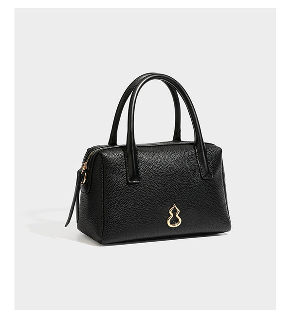 Small structured pillow satchel bag with pebbled leather-look finish, dual rolled top handles, gold-tone gourd emblem, and