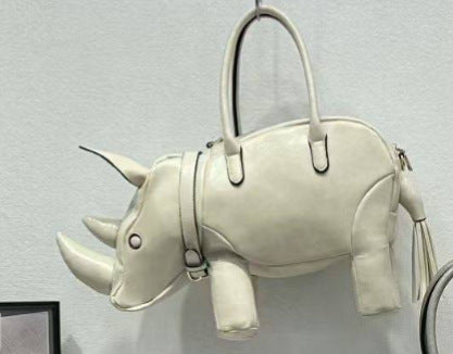 Rhinoceros-shaped 3D structured handbag with sculpted horns, four legs, tassel tail, twin top handles, and detachable, detail