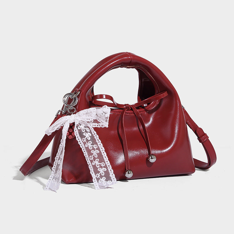 Small glossy leather-look dome top-handle bag with drawstring tie closure, white lace bow charm, and silver-tone hardware