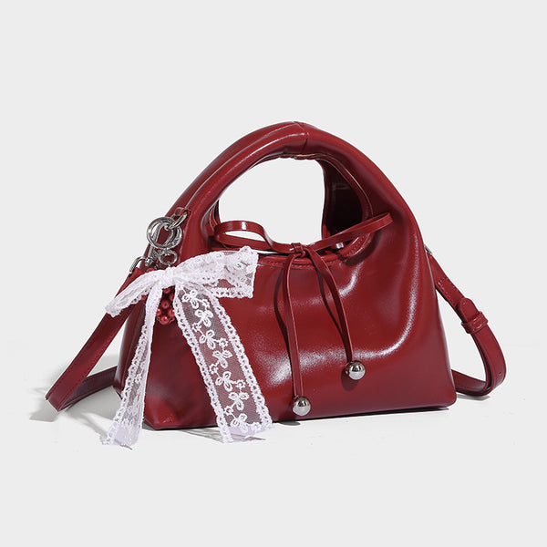 Kleine glänzende kuppelförmige Henkeltasche in Lederoptik mit Zugbandverschluss, weißem Spitzen-Schleifenanhänger und silberfarbenen Beschlägen